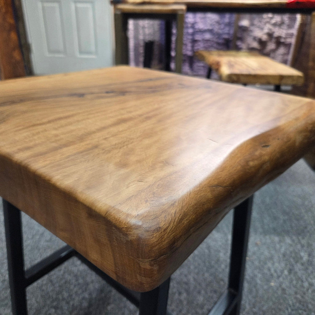 close up A rustic live-edge Live Oak end table with a square top and black metal legs, photographed on a gray carpeted floor.