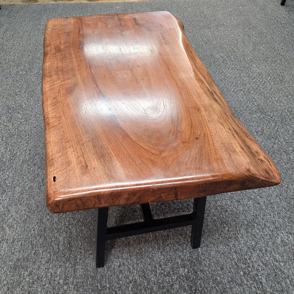 A live-edge wooden coffee table with a glossy, polished brown wood top and black metal legs, photographed on a gray carpeted floor.