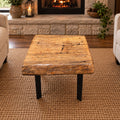 Handcrafted pecan coffee table with natural wood character and black metal legs staged between two chairs in front of a fireplace.