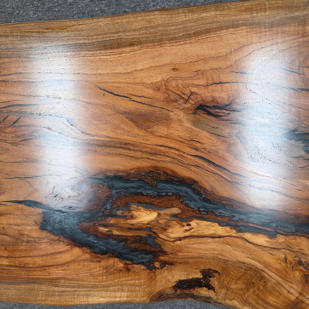 Handcrafted live edge wood table with black epoxy-filled voids and custom black metal base