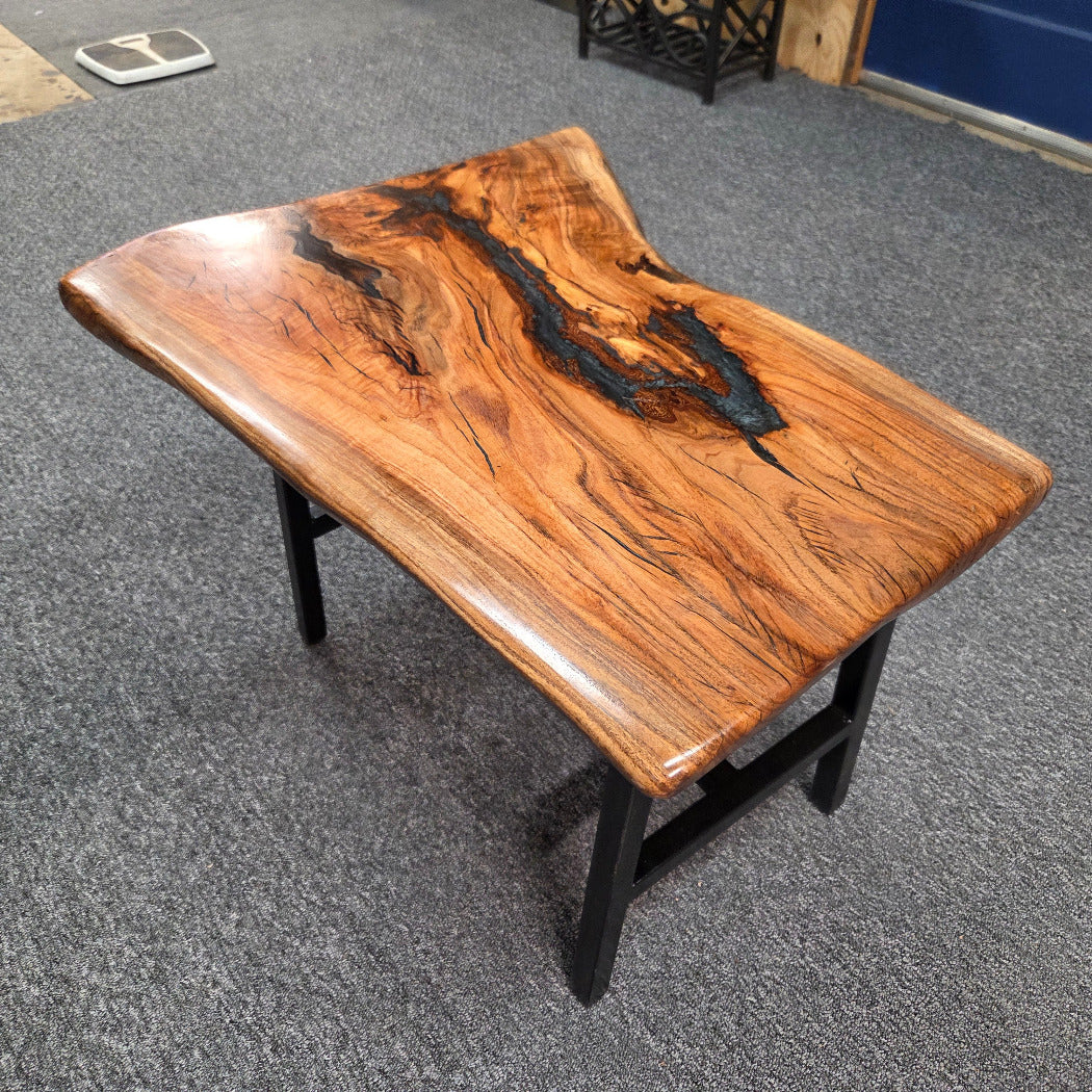 Handcrafted live edge wood table with black epoxy-filled voids and custom black metal base