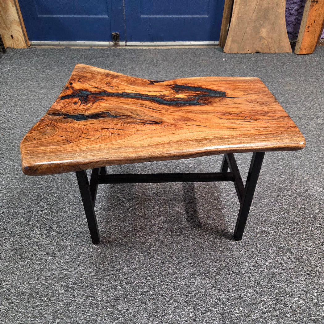 Handcrafted live edge wood table with black epoxy-filled voids and custom black metal base