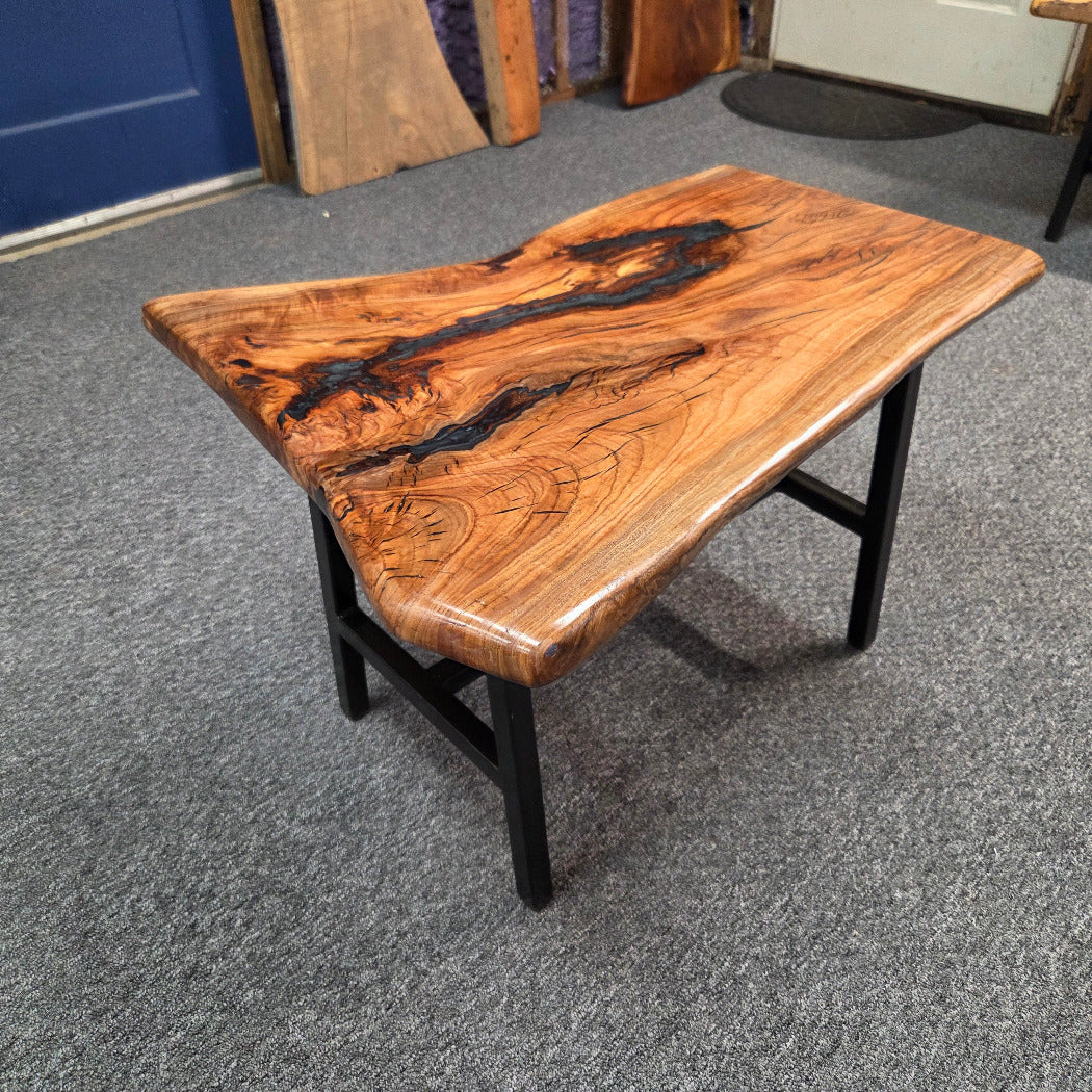 Handcrafted live edge wood table with black epoxy-filled voids and custom black metal base