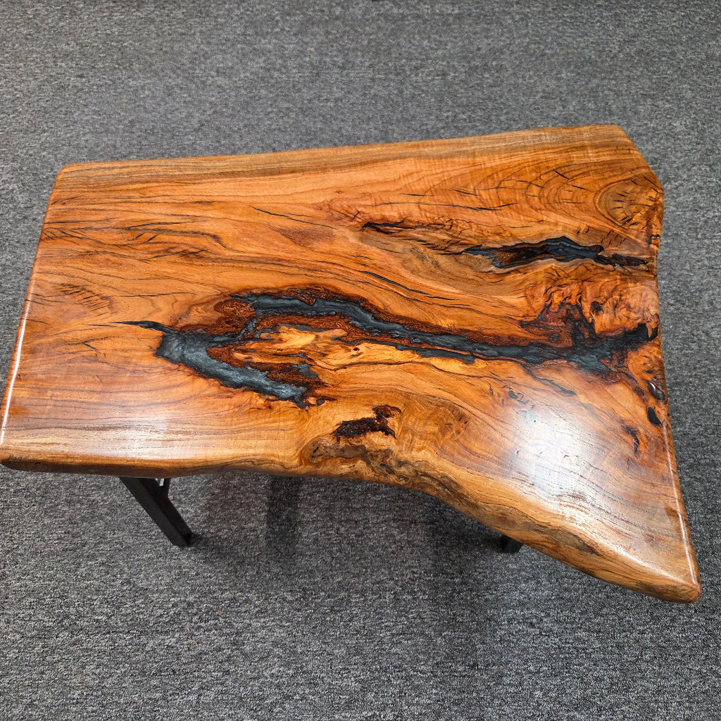 Handcrafted live edge wood table with black epoxy-filled voids and custom black metal base