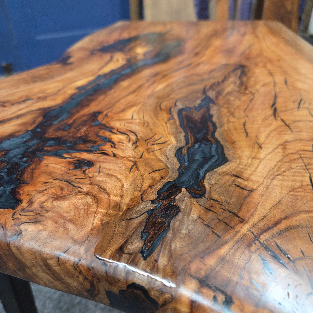 Handcrafted live edge wood table with black epoxy-filled voids and custom black metal base
