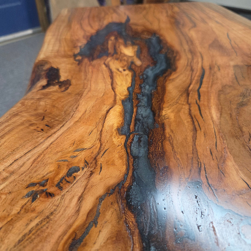 Handcrafted live edge wood table with black epoxy-filled voids and custom black metal base