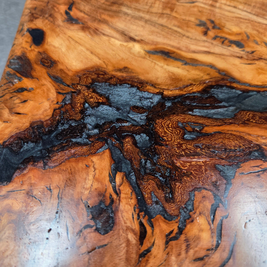Handcrafted live edge wood table with black epoxy-filled voids and custom black metal base