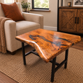 A rustic live-edge wooden coffee table with a glossy, polished surface showing rich natural grain and dark resin pockets, supported by a black metal frame. The table is styled in a cozy living room setting next to a beige armchair and on a woven jute rug.