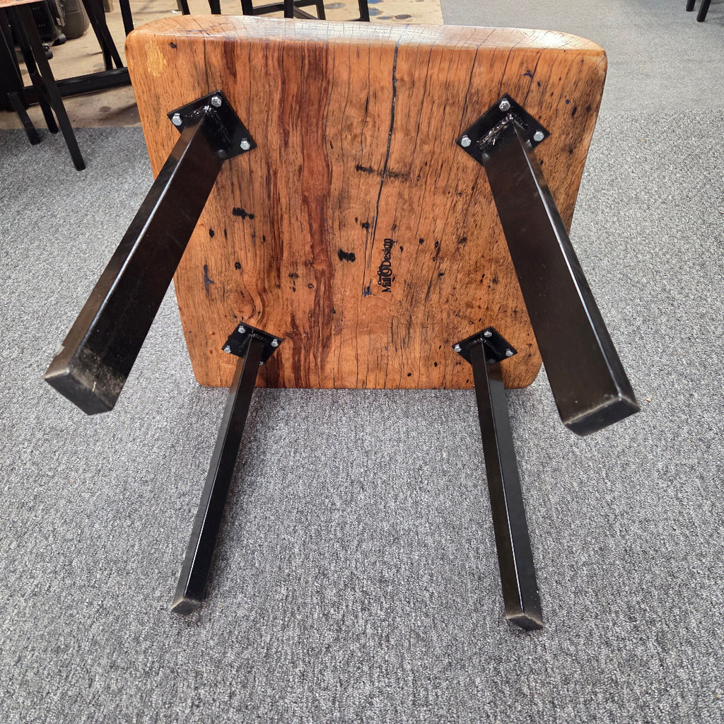 bottom view Handcrafted pecan coffee table with natural wood character and black metal legs staged between two chairs in front of a fireplace.