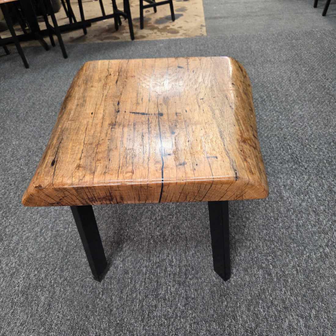 Handcrafted pecan coffee table with natural wood character and black metal legs staged between two chairs in front of a fireplace.