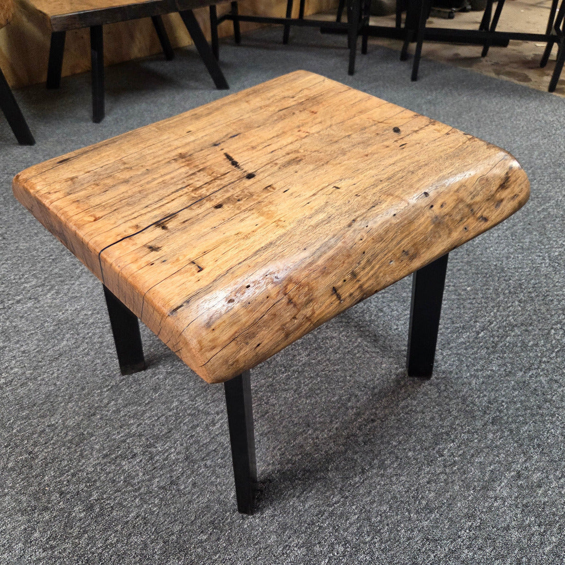Handcrafted pecan coffee table with natural wood character and black metal legs staged between two chairs in front of a fireplace.