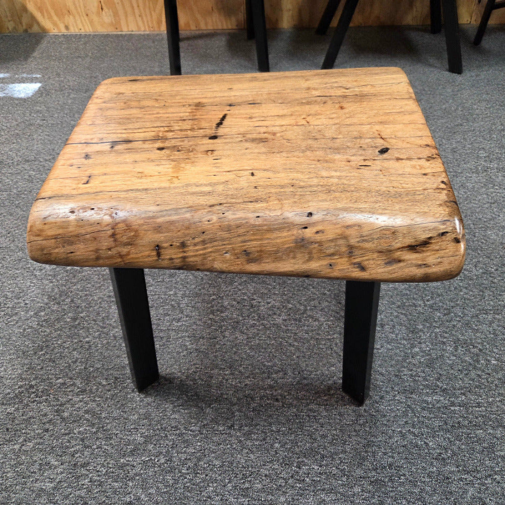 Handcrafted pecan coffee table with natural wood character and black metal legs staged between two chairs in front of a fireplace.