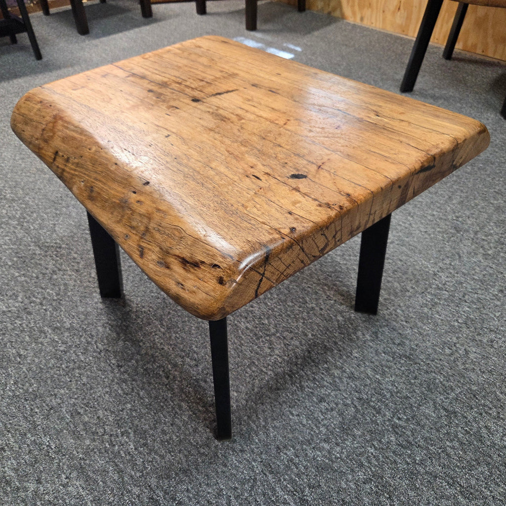 Handcrafted pecan coffee table with natural wood character and black metal legs staged between two chairs in front of a fireplace.