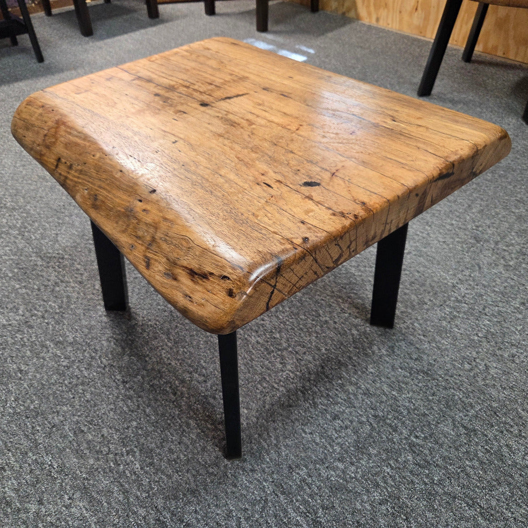 Handcrafted pecan coffee table with natural wood character and black metal legs staged between two chairs in front of a fireplace.