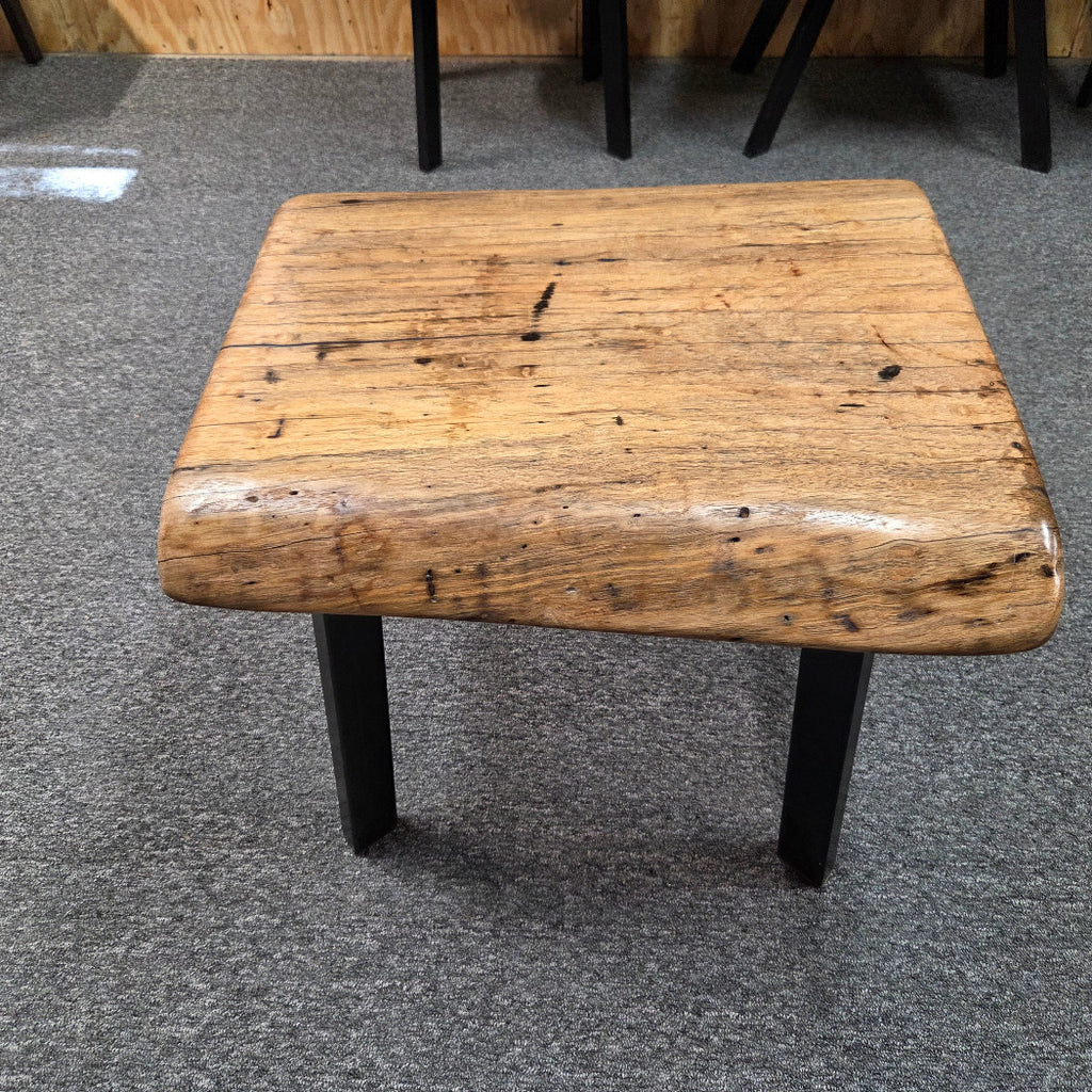 Handcrafted pecan coffee table with natural wood character and black metal legs staged between two chairs in front of a fireplace.