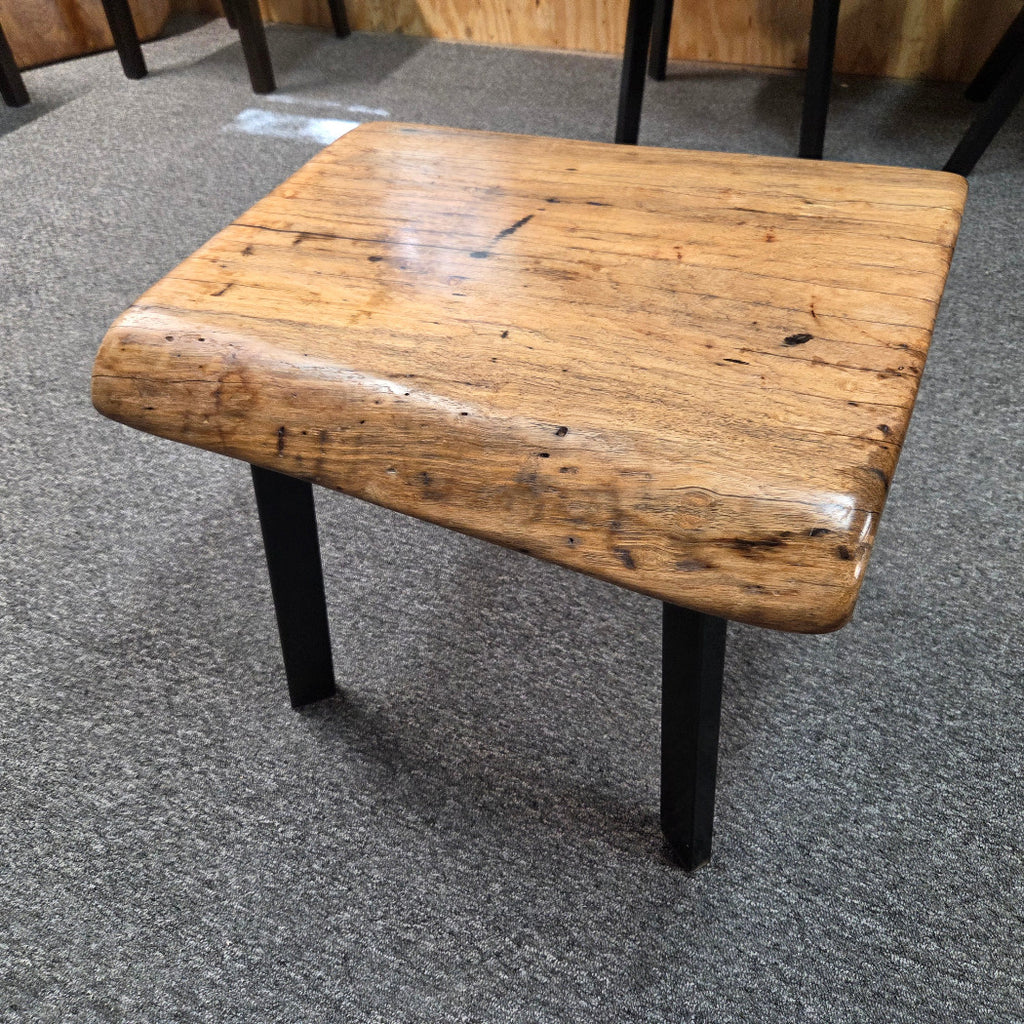 Handcrafted pecan coffee table with natural wood character and black metal legs staged between two chairs in front of a fireplace.