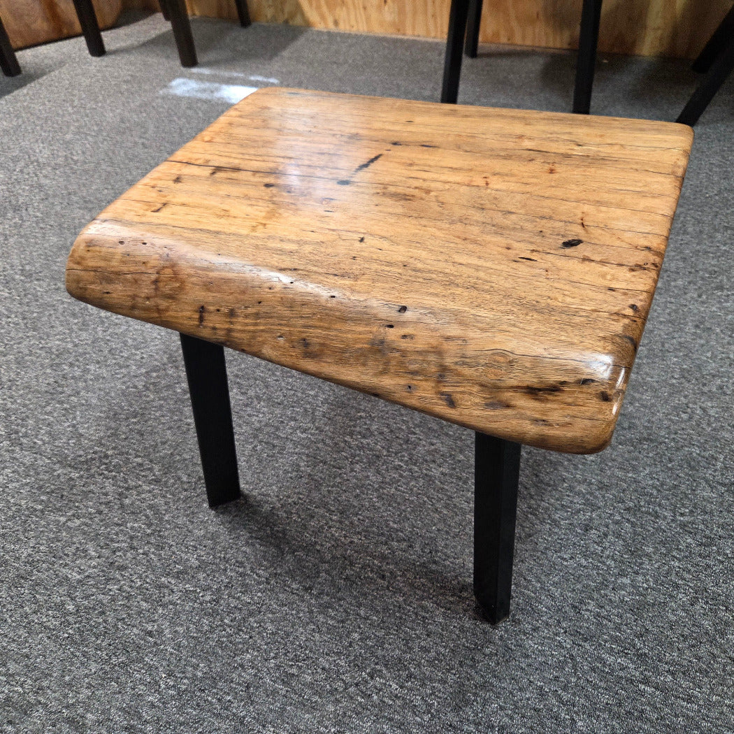 Handcrafted pecan coffee table with natural wood character and black metal legs staged between two chairs in front of a fireplace.