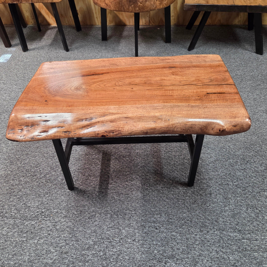 A live-edge wooden coffee table with a glossy finish and black metal legs, set on a gray carpeted floor.