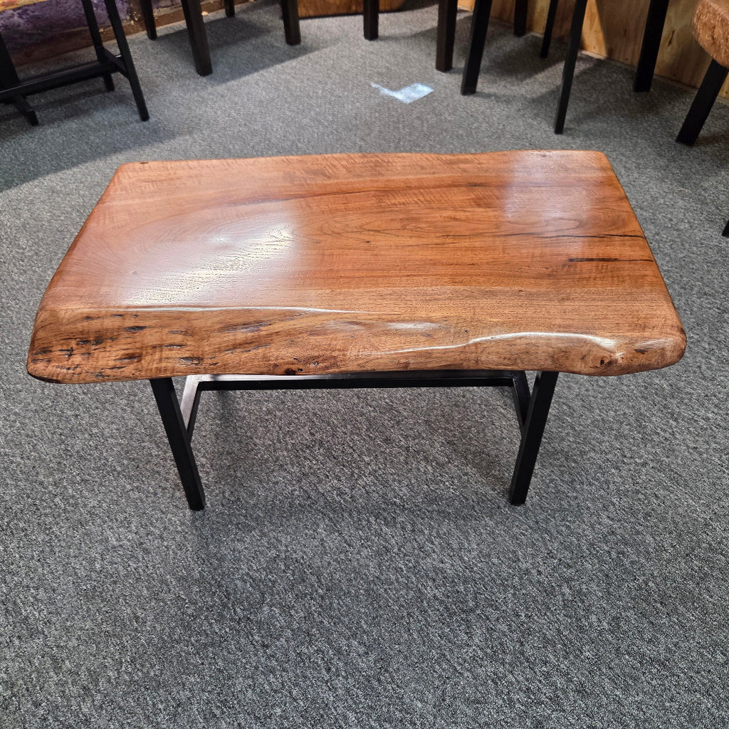 A rectangular live-edge wooden coffee table with a glossy brown finish and black metal legs, shown on a gray carpeted floor.