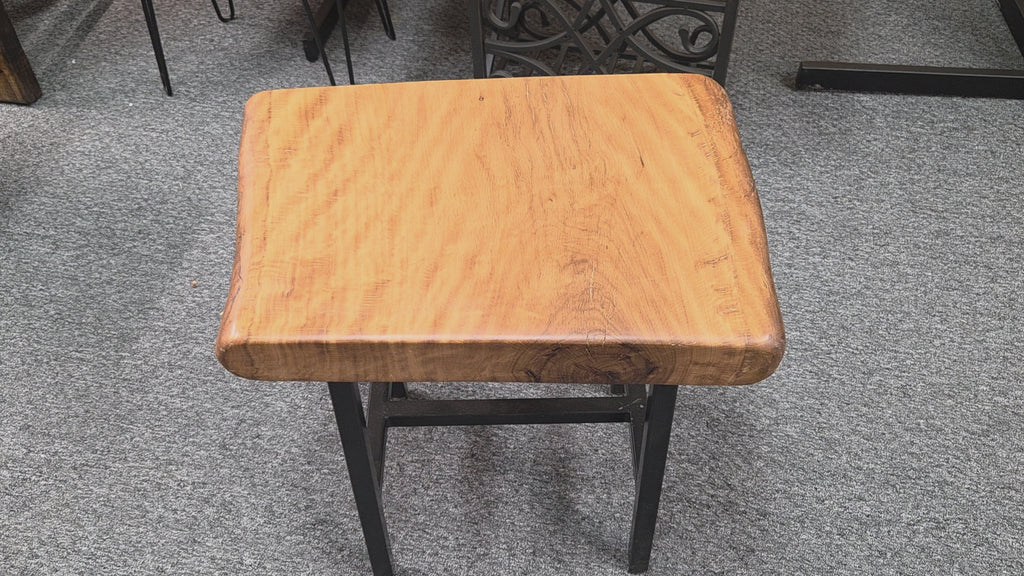 A rustic Live Oak end table with a thick, live-edge natural wood seat and a black metal frame, set on a gray carpeted floor.