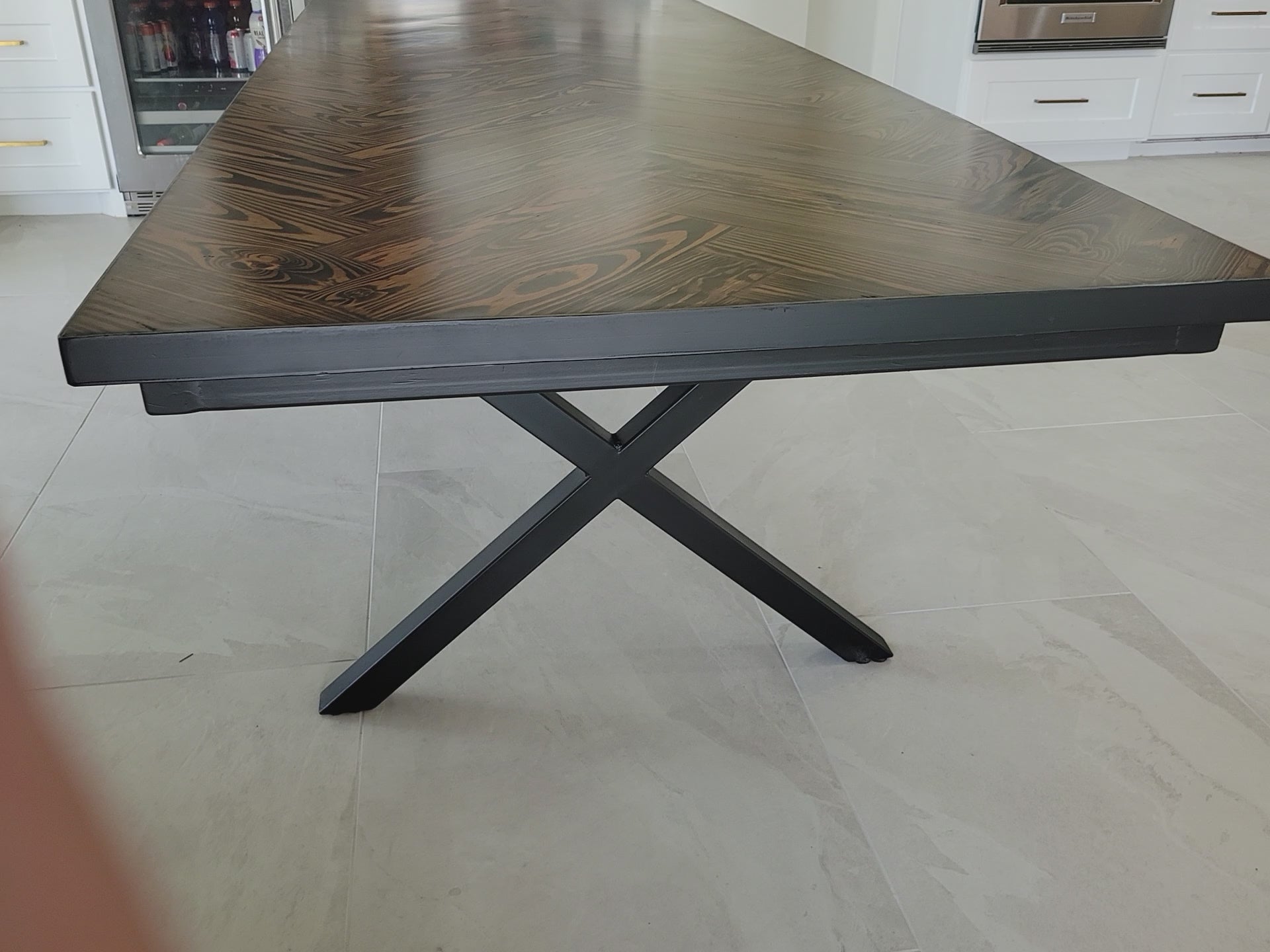 A rectangular long leaf pine dining table with a dark brown herringbone pattern top and black metal legs and metal sides shown in a home interior setting.