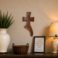 A styled interior scene showing a dark wood console table against a beige wall, with a large white vase holding a green plant on the left, a small wicker basket in the center, a framed scripture print, and a lit table lamp on the right.